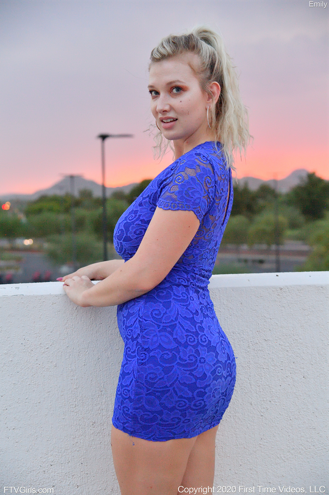 teen pornstar Emily FTV is non nude wearing a blue sexy fit dress while standing beside a wall in Sunset Finale