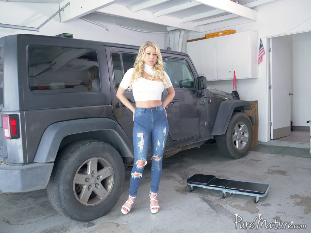 pornstar Katie Morgan is standing near a car while wearing a tattered jeans and white shirt in a garage in Lets Workout A Deal
